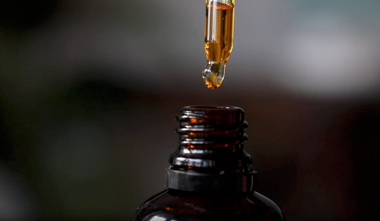 a pipette dropping an oil into a brown, amber glass bottle