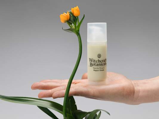 Witchcraft Botanicals Matcha Miracle Repair Cream on a palm with an orange flower next to it