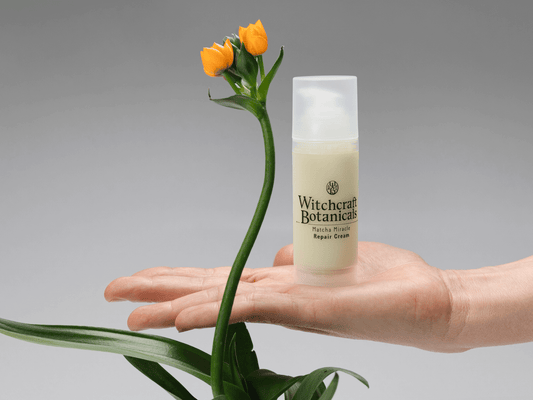 Witchcraft Botanicals Matcha Miracle Repair Cream on a palm with an orange flower next to it